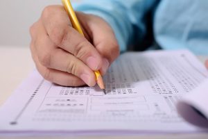 person holding a pencil and filling in a multiple choice scantron sheet