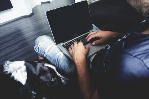 Man typing at laptop with dog next to him